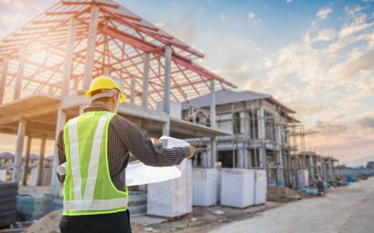 Professional engineer architect worker with protective helmet and blueprints paper at house building construction site